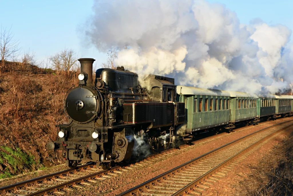 Vintage steam train running on railway tracks with smoke clouds in the background